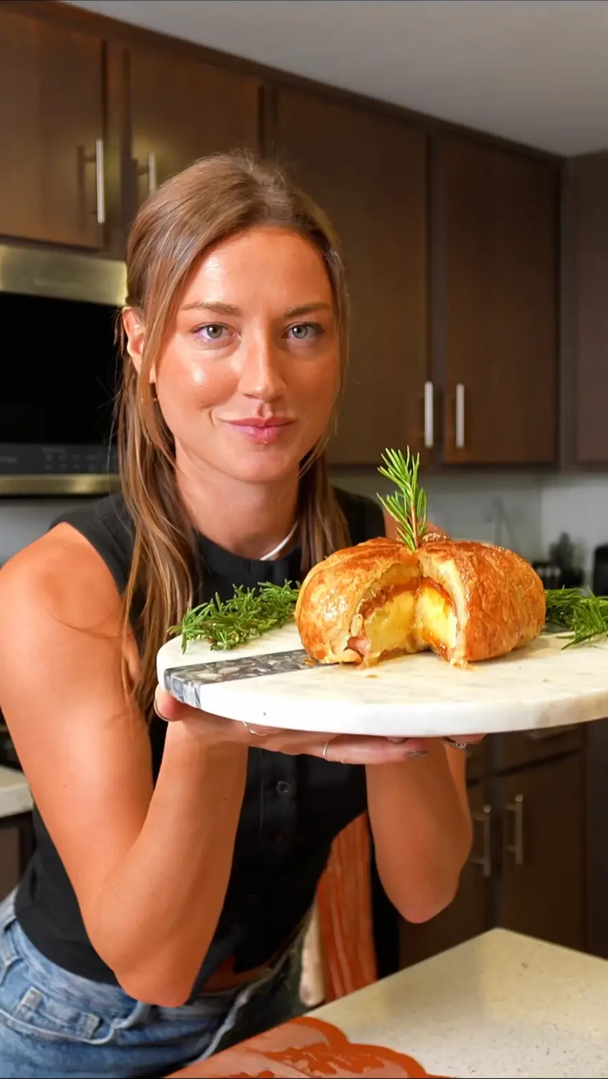Corinne holding a pastry board with a baked pastry and rosemary